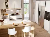 Modern white kitchen with a wooden island, bar stools, stainless steel fridge, and oven.