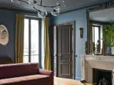Soggiorno elegante con divano bordeaux, pareti blu balena e tendaggi dorati. Un camino in marmo e sculture africane completano l'arredo.