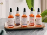 Cinque flaconi di oli naturali per il viso, con contagocce, disposti su un vassoio di legno.