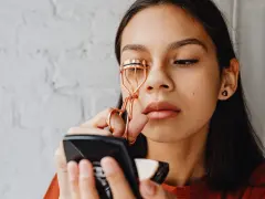 Ragazza usa un piegaciglia dorato, sperando che non rovina le ciglia.