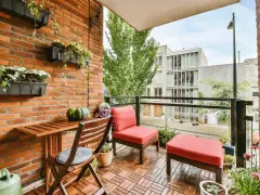 Arredare terrazzo appartamento: un angolo relax con sedie rosse, tavolino in legno e piante su muro di mattoni.