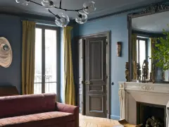 Soggiorno elegante con divano bordeaux, pareti blu balena e tendaggi dorati. Un camino in marmo e sculture africane completano l'arredo.