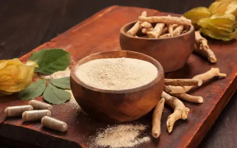 Radici, polvere e capsule di ashwagandha su tagliere di legno. Scopri come assumere ashwagandha per il benessere.