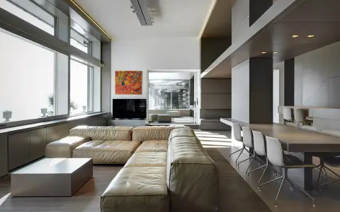 Un ampio soggiorno moderno, perfetto per arredare soggiorno grande, con divano componibile in pelle chiara, tavolino squadrato e zona pranzo con tavolo lungo e sedie di design.