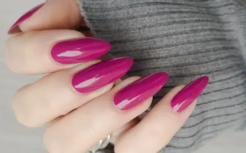 Mano con unghie lunghe e affusolate, smalto color ciliegia brillante, su sfondo grigio melange.
