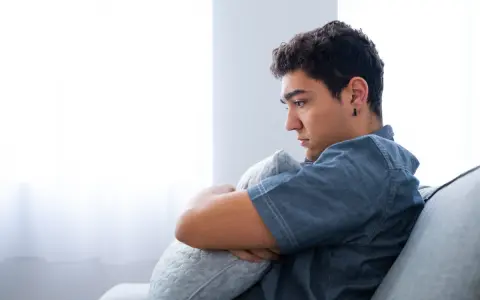 Ragazzo pensieroso abbraccia un cuscino, riflettendo sull'insonnia adolescenza rimedi naturali.