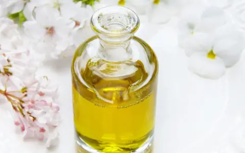 Flacone di vetro con liquido dorato, circondato da fiori bianchi e rosa. Un invito a pensare a dove buttare profumi pieni.