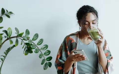 Donna con capelli ricci beve un tè verde mentre guarda il telefono, ignara che il tè fa ingrassare.