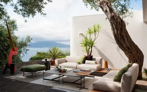 Arredare un terrazzo scoperto con divani chiari, tavolini geometrici e un pouf verde. Vista mare e scultura astratta.