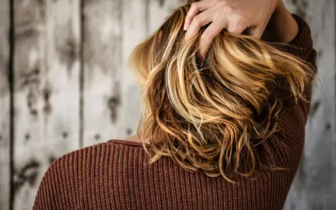 Mano tra i capelli biondi e mossi, che ricadono morbidi sulle spalle.