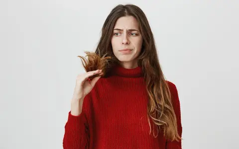 Donna preoccupata guarda le doppie punte, pensando a come nutrire i capelli per renderli sani e forti.