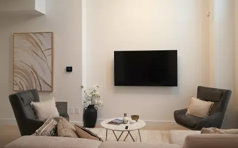 Soggiorno con TV a parete, divano, poltrone e tavolino. L'arredamento minimalista crea un'atmosfera rilassante.