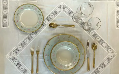 Tavola apparecchiata con piatti azzurri decorati con farfalle rosa e fiocchi, posate dorate e bicchieri eleganti. Idee tavola apparecchiata per un'occasione speciale.