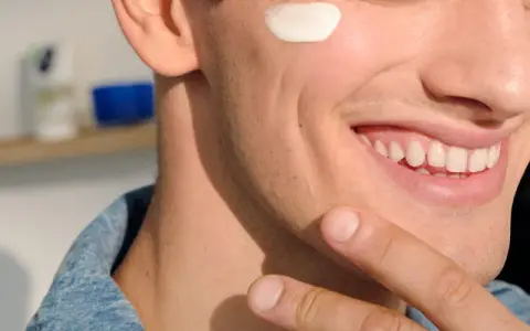 Uomo sorridente con crema sul viso, dopo la depilazione con rasoio. Pelle liscia e curata.