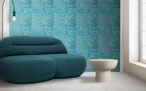Divano blu petrolio davanti a una parete con motivo floreale su sfondo colore verde acqua. Tavolino beige e lampada nera.