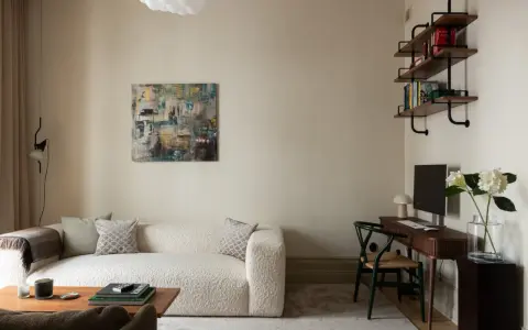 Soggiorno accogliente con divano bouclé bianco, quadro astratto e scrivania. Le **pareti colore crema** creano un'atmosfera calda e rilassante.