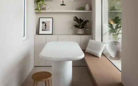Un angolo accogliente con tavolo bianco, sgabello in legno e piante. Un'ispirazione su come combattere la solitudine in casa, creando spazi piacevoli.