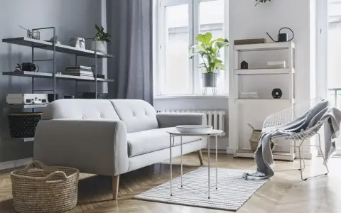 Soggiorno moderno con divano grigio, tavolino bianco, cestini in paglia e scaffali pieni di oggetti. Ottime idee arredamento casa per uno stile minimalista.