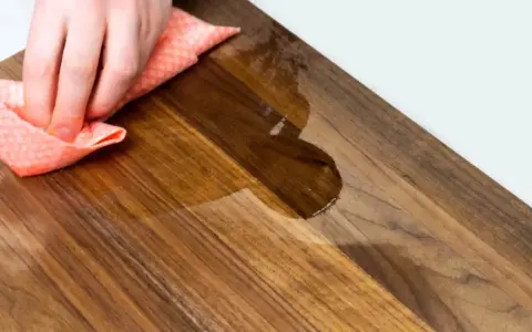 Mano che pulisce un tagliere di legno con un panno umido. Scopri come pulire il tagliere di legno per mantenerlo igienico e bello.