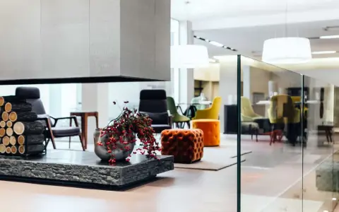 Interni open space di case moderne: camino con legna, vasi con bacche rosse, sedie colorate e pouf arancioni in un ambiente luminoso.