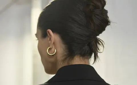 Capelli scuri raccolti in un chignon semplice, con un orecchino a cerchio dorato.