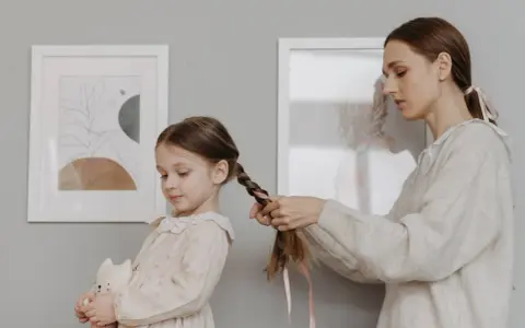 Mamma intreccia i capelli della bambina, creando bellissime acconciature. La piccola tiene un pupazzo a forma di gatto.