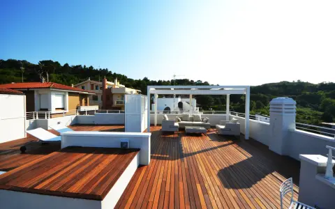Terrazza sul tetto idee: un salotto all'aperto con divani, poltrone e tavolino sotto un pergolato bianco. Sdraio e vista su case e colline verdi.