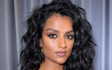 Capelli neri e ondulati, lucidi grazie al hair oiling, incorniciano il viso di una donna con trucco intenso.