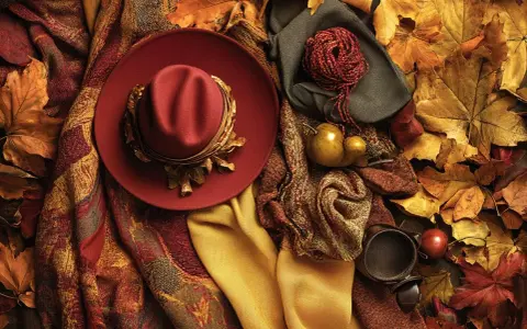 Cappello rosso, sciarpe, gomitolo e foglie autunnali creano un'atmosfera con **colori caldi**.