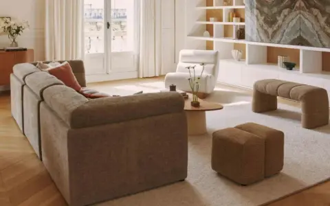 Soggiorno con divano componibile, poltrona, pouf e panca. Arredamento casa stile moderno con mobili in legno e tessuti neutri.