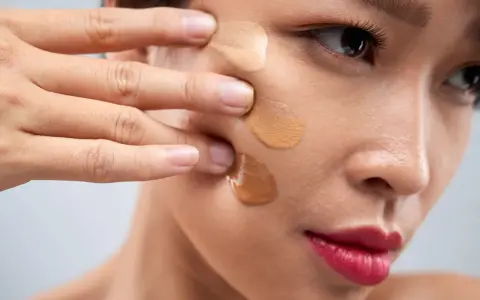 Dita che sfumano campioni di fondotinta sulla guancia per capire come scegliere il colore del fondotinta perfetto.