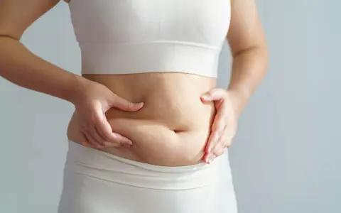 Mani che stringono la pancia, segno di accumulo adiposo. Potrebbe essere una pancia da cortisolo alto, legata allo stress.