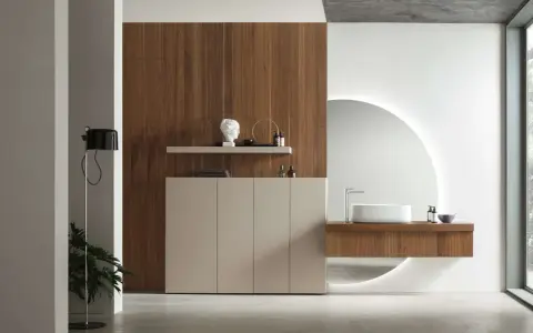 Bagno elegante e raffinato con mobile in legno, lavabo sospeso, specchio circolare retroilluminato e un tocco di verde da una pianta.