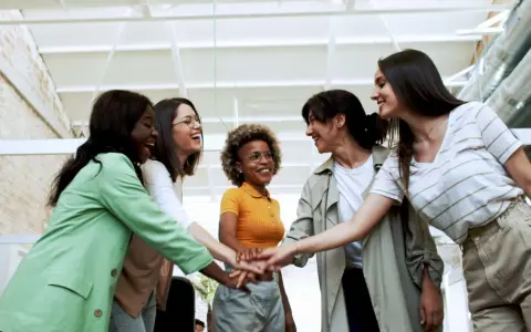 Cinque donne sorridono, unendo le mani in un gesto di unione e **empowerment femminile**.