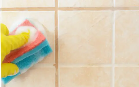Mano con guanto giallo pulisce piastrelle del bagno con spugna schiumosa.