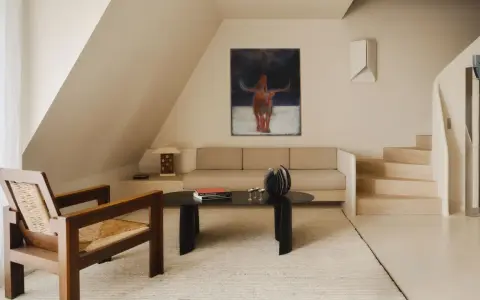 Arredamento minimal soggiorno: poltrona in legno e paglia, divano beige, tavolino nero con libri e scultura, quadro astratto con toro.