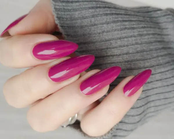 Mano con unghie lunghe e affusolate, smalto color ciliegia brillante, su sfondo grigio melange.