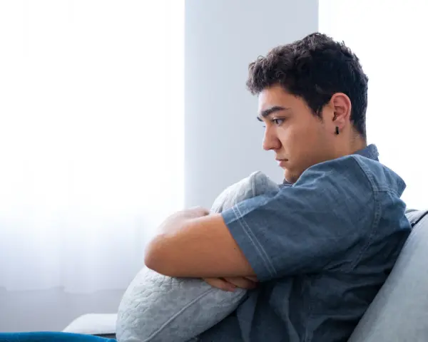 Ragazzo pensieroso abbraccia un cuscino, riflettendo sull'insonnia adolescenza rimedi naturali.