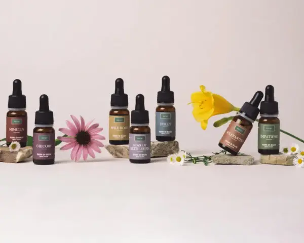Flaconi di Fiori di Bach Rescue Remedy con Mimulus, Chicory, Wild Rose, Star of Bethlehem, Holly, Scleranthus e Impatiens, circondati da fiori.