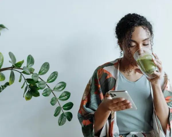 Donna con capelli ricci beve un tè verde mentre guarda il telefono, ignara che il tè fa ingrassare.