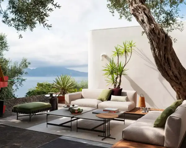Arredare un terrazzo scoperto con divani chiari, tavolini geometrici e un pouf verde. Vista mare e scultura astratta.