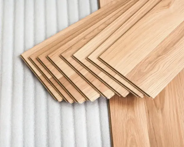 Assortimento di listoni di legno betulla colore chiaro, pronti per essere posati su un tappeto protettivo bianco.