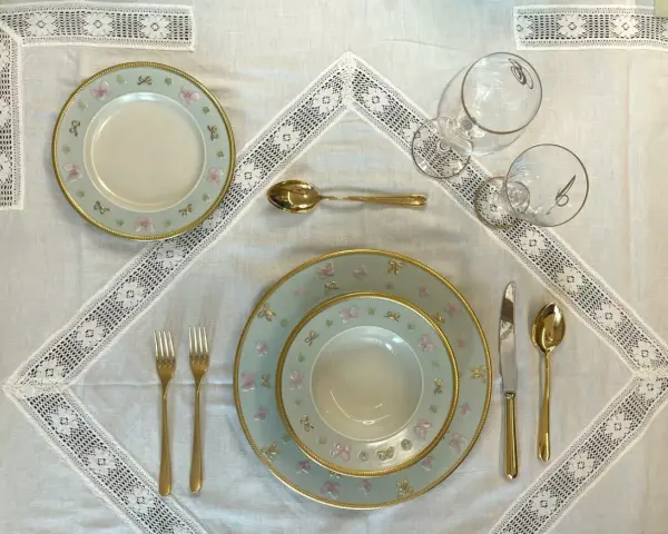 Tavola apparecchiata con piatti azzurri decorati con farfalle rosa e fiocchi, posate dorate e bicchieri eleganti. Idee tavola apparecchiata per un'occasione speciale.