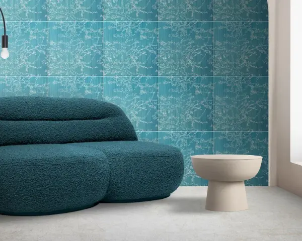 Divano blu petrolio davanti a una parete con motivo floreale su sfondo colore verde acqua. Tavolino beige e lampada nera.