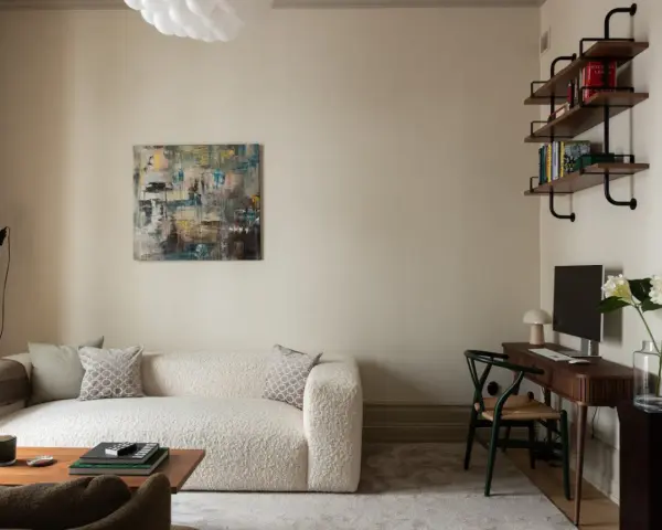 Soggiorno accogliente con divano bouclé bianco, quadro astratto e scrivania. Le **pareti colore crema** creano un'atmosfera calda e rilassante.