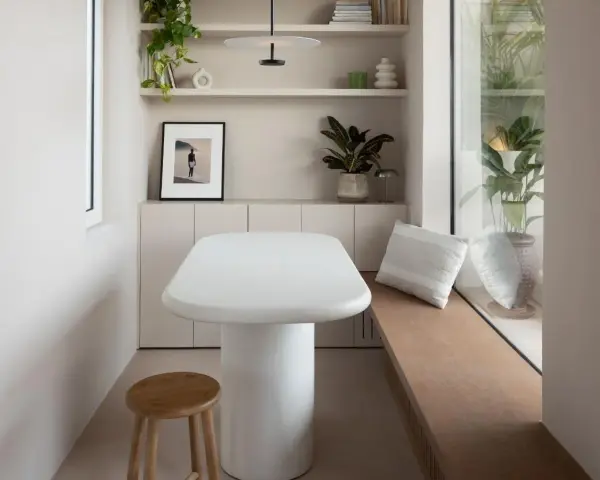Un angolo accogliente con tavolo bianco, sgabello in legno e piante. Un'ispirazione su come combattere la solitudine in casa, creando spazi piacevoli.