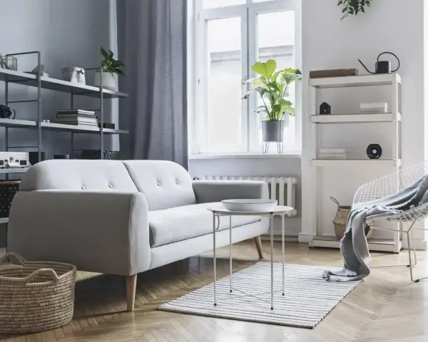 Soggiorno moderno con divano grigio, tavolino bianco, cestini in paglia e scaffali pieni di oggetti. Ottime idee arredamento casa per uno stile minimalista.