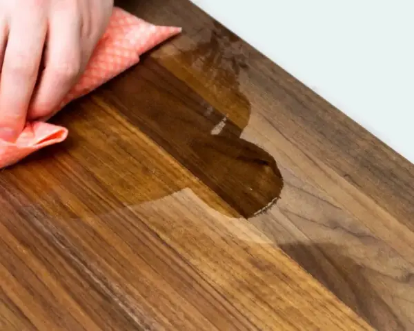 Mano che pulisce un tagliere di legno con un panno umido. Scopri come pulire il tagliere di legno per mantenerlo igienico e bello.