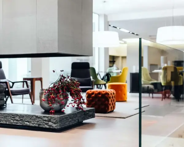Interni open space di case moderne: camino con legna, vasi con bacche rosse, sedie colorate e pouf arancioni in un ambiente luminoso.
