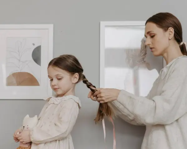 Mamma intreccia i capelli della bambina, creando bellissime acconciature. La piccola tiene un pupazzo a forma di gatto.